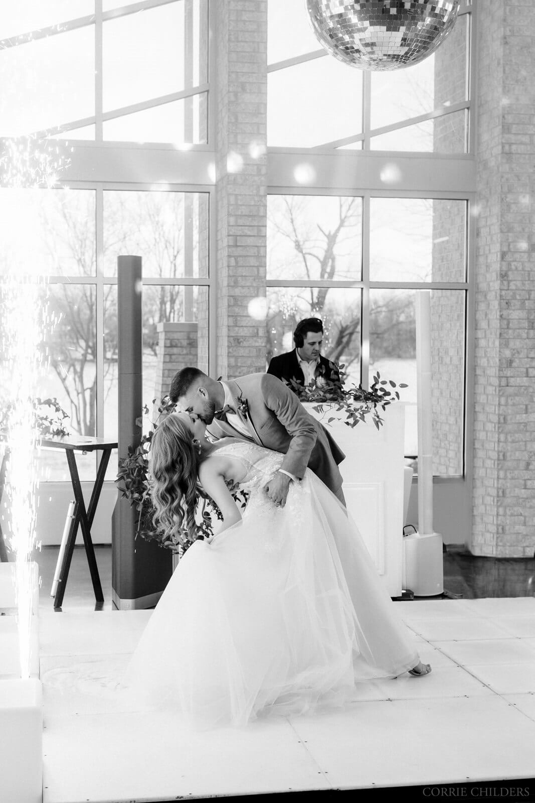 Groom dipping bride, kissing on the dance floor with Ozark Mix DJ booth in background